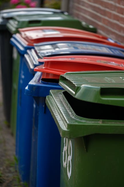 A large green wheeled waste disposal bin with the number 53 and the words 'JUN BESAR' printed on its side, positioned on the pavement outside a residential property. To the left of the bin, there is a