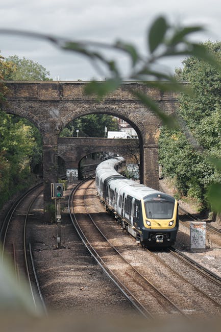 View of Putney railway station platform with yellow tactile paving along the edge, metal overhead canopy structure, and a brick station building with multiple glass windows on the left side. The platf